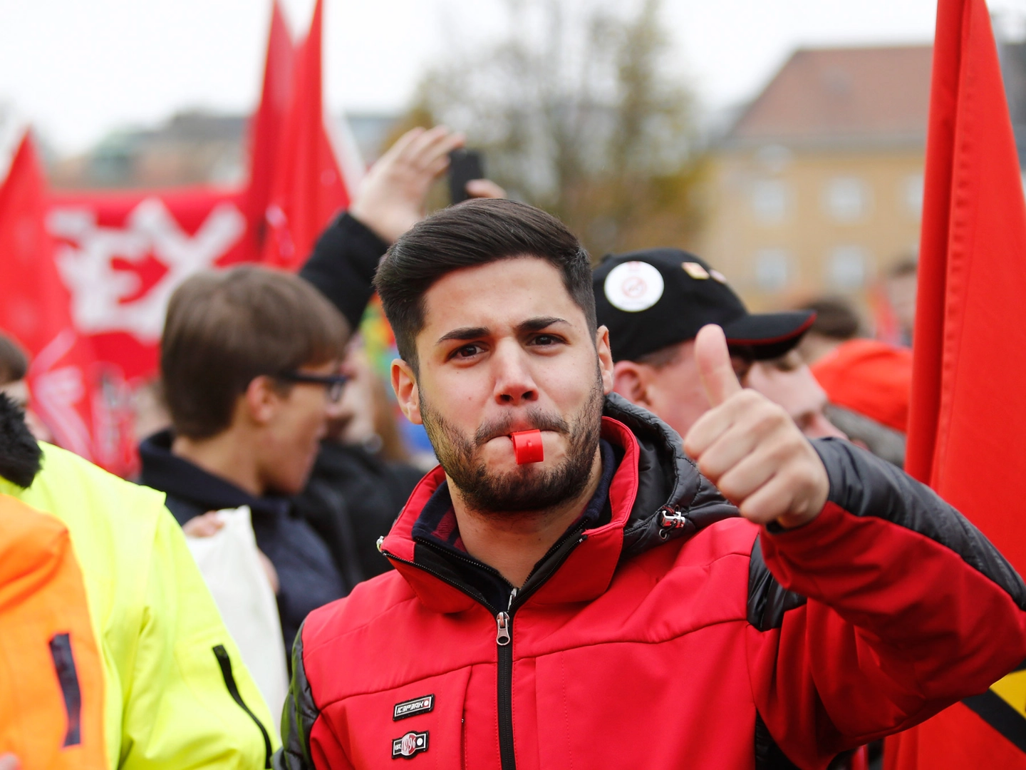 Ein junger Mann mit roter Jacke und Trillerpfeife streckt den Daumen nach oben.