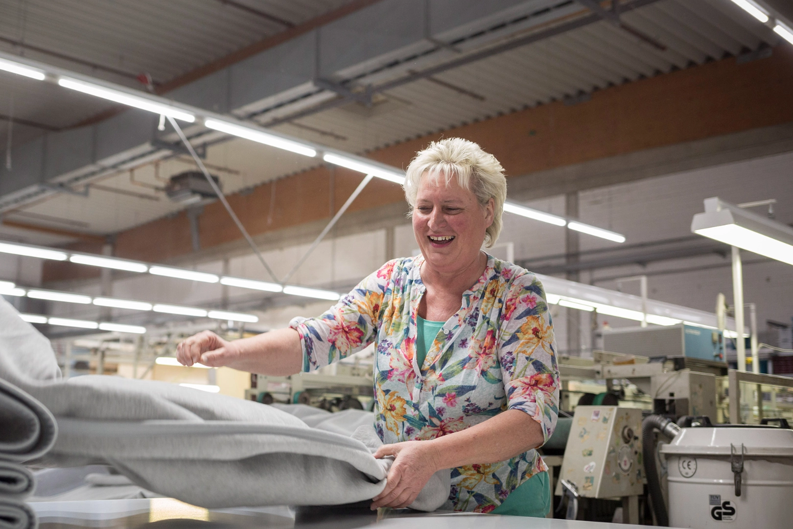 Eine Frau mit Blonden kurzen Haaren wirft lachend eine Stoffbahn aus.