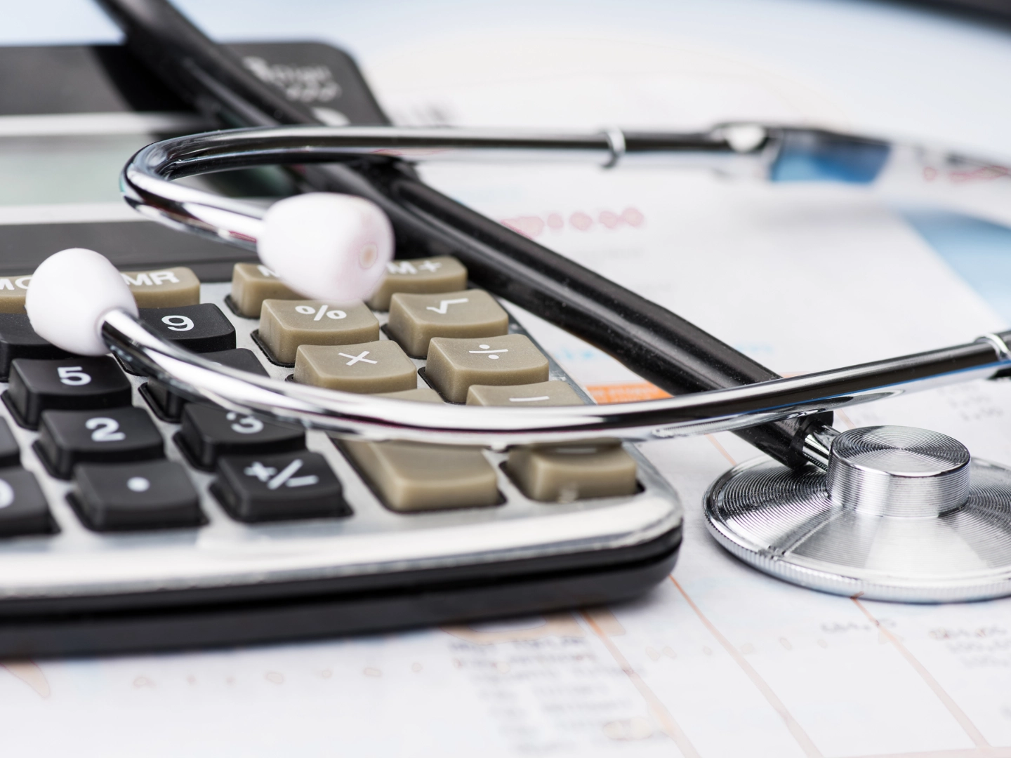Ein Stethoskop liegt auf einem Taschenrechner und Unterlagen