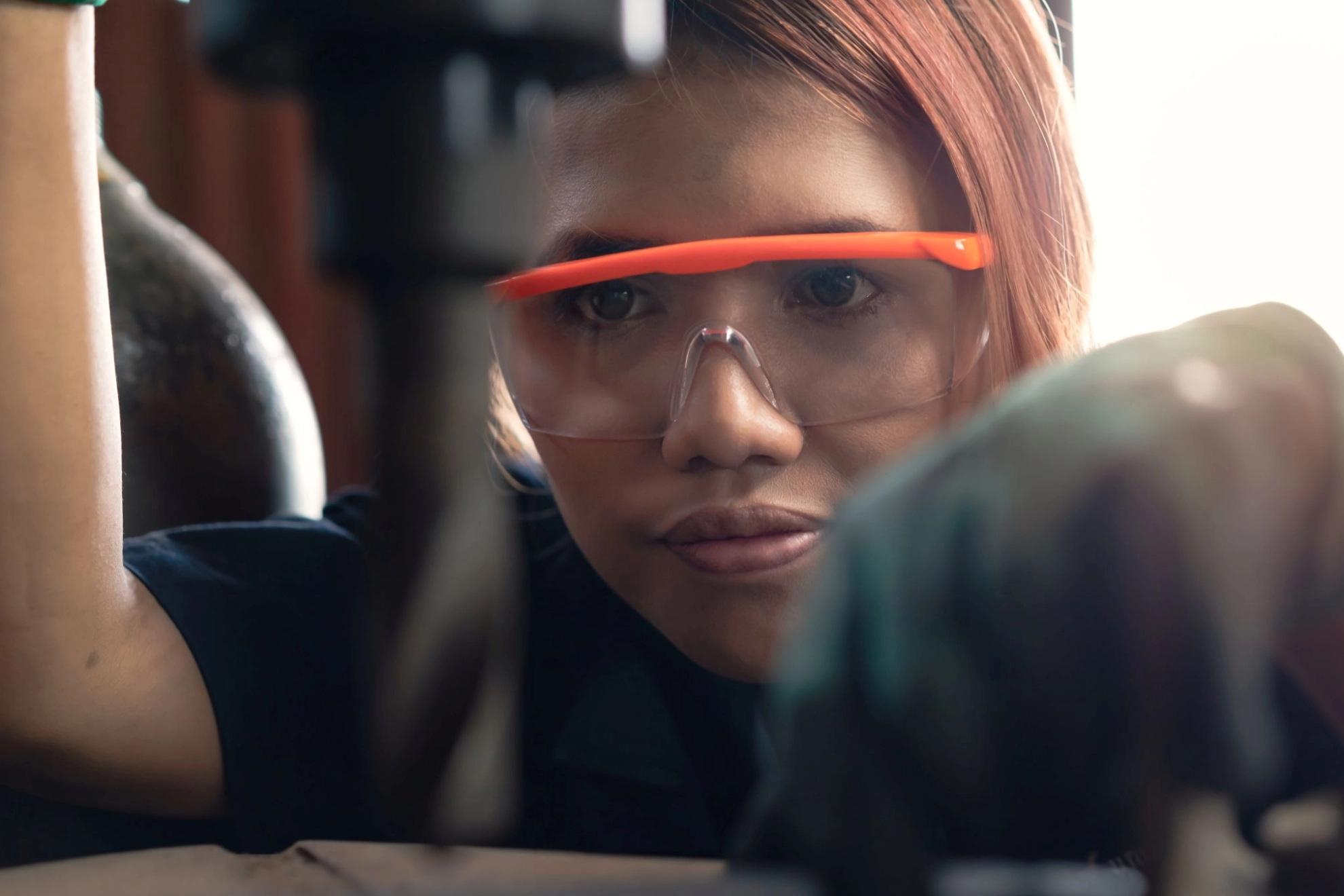 junge Frau arbeitet in einer Werkstatt mit Schutzbrille