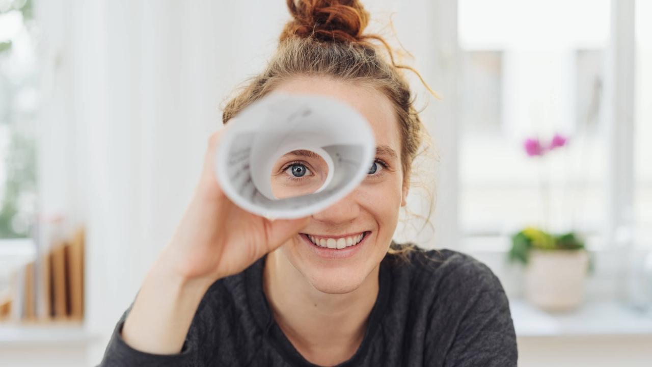 Eine junge Frau blickt durch ein gerolltes Blatt Papier.