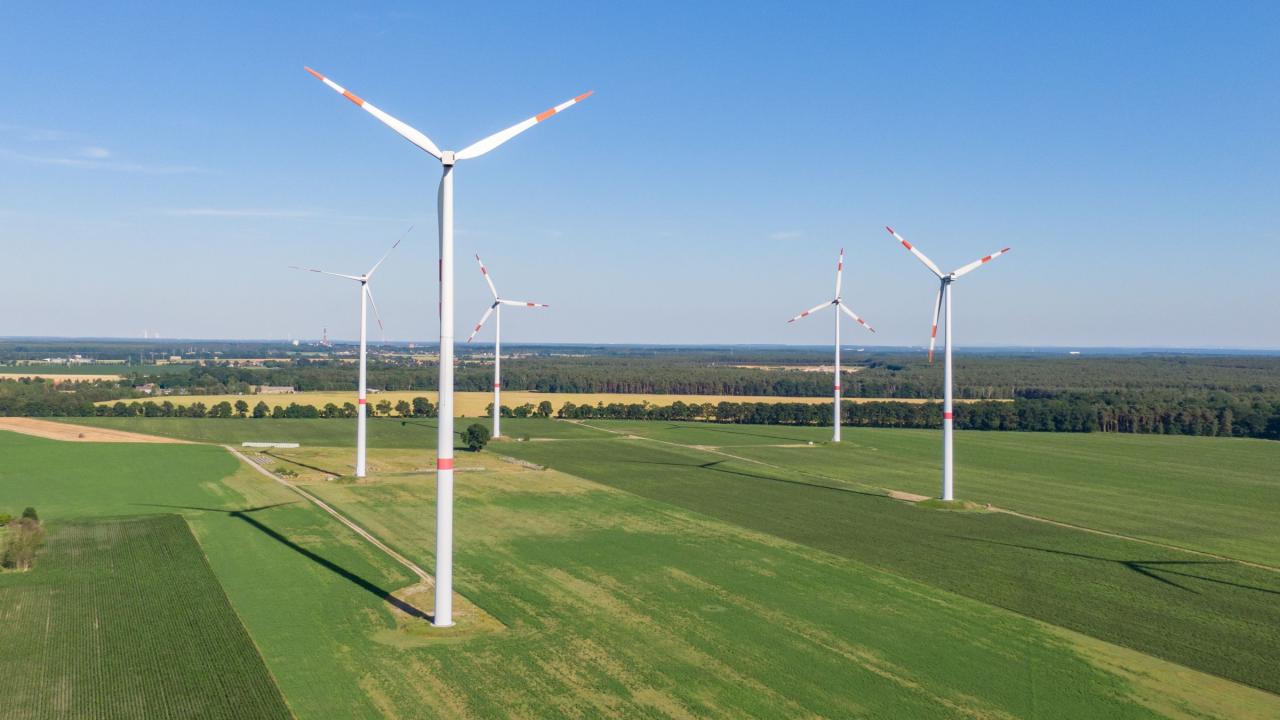 mehrere Windkraftanlagen bei gutem Wetter auf grüner Wiese